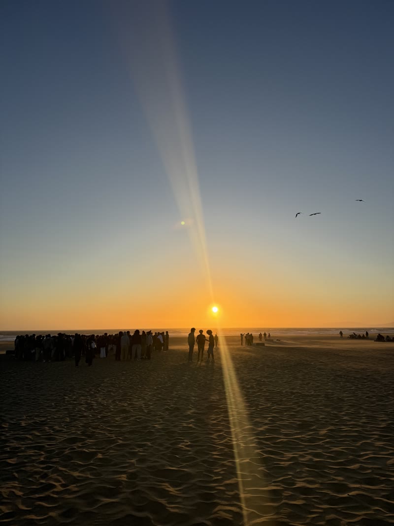 A crowd gathered on a beach watching the sun set over the ocean